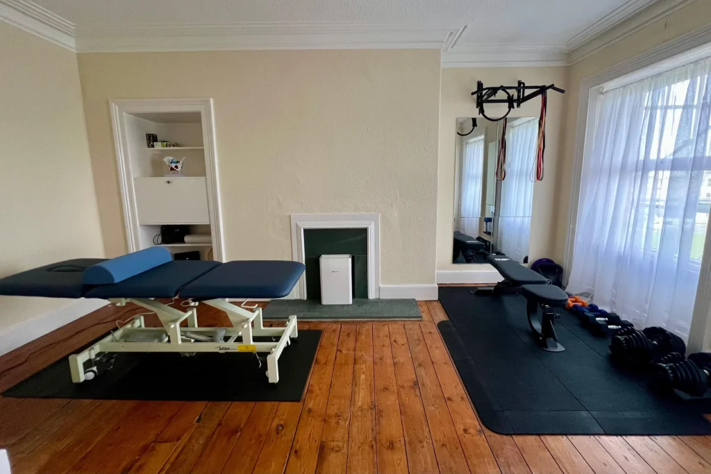 Private women’s health clinic room in Tynemouth with physio treatment bed, rehab gym bench, weights and bright natural light